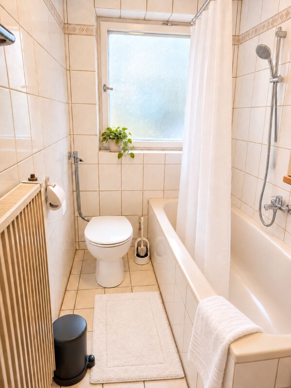 A bathroom with a toilet, a shower, a bathtub, a window with a plant, and a radiator. - Apartment Albert: Quiet vacation rental right on the Altmühl *air-conditioned* (Pappenheim)