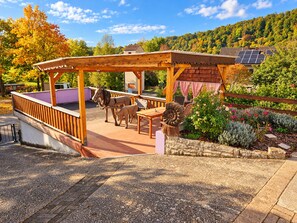 Eine hölzerne Pergola mit Sitzgelegenheiten, eine Pferdestatue und ein Garten mit verschiedenen Pflanzen.
