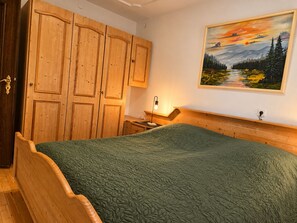 A bedroom with a wooden wardrobe, a bed with a green quilt, a bedside table with a lamp, and a painting of a landscape on the wall. - Albert Apartment: Quiet Vacation Rental on the Banks of the Altmühl *Air-Conditioned* (Pappenheim)