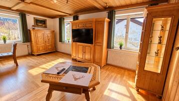 A wooden-paneled room with a television, a cabinet with glass doors, a table with a placemat, and a window with a view of the outdoors.
