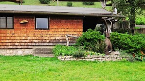 Ein rustikales Holzhaus mit Steinunterbau, ein kleiner Garten mit verschiedenen Pflanzen und eine Sat-Anlage auf dem Dach.