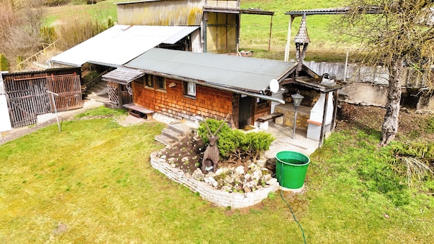 Ein rustikales Holzhaus mit geneigtem Dach, einem Steinuntergrund und einem kleinen Garten mit einem grünen Eimer.