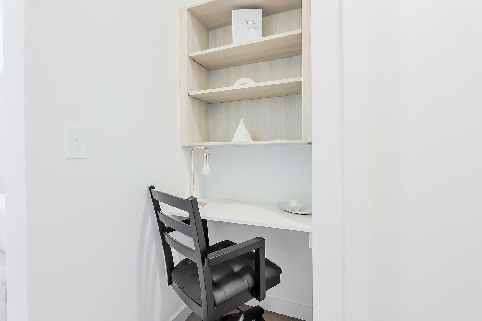 A white room with a desk, a chair, and a shelf with a sign.