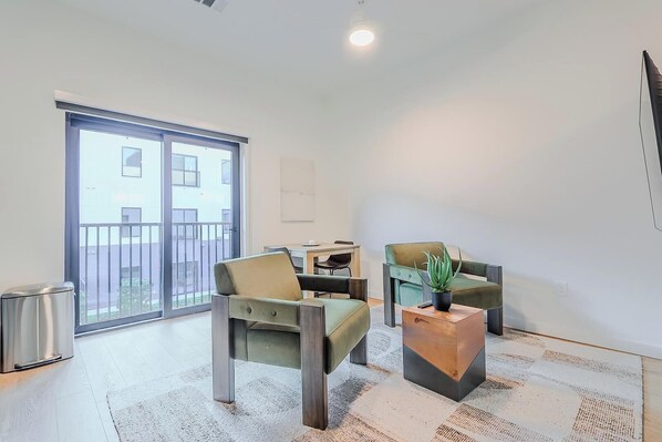 A modern living room with a sofa, armchair, and a small table with a plant. There is a sliding glass door leading to a balcony. - Landing | Spectacular Studio, Courtyard, Gym (Houston)