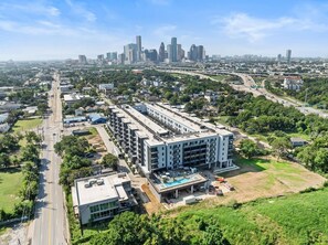 A multi-story building with a rooftop pool, surrounded by greenery and a city skyline in the background. - Landing | Spectacular Studio, Courtyard, Gym (Houston)