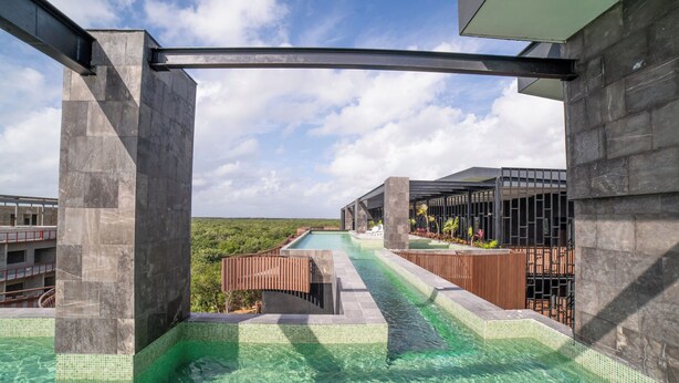 A pool area with clear water, surrounded by stone walls and a wooden bridge. - 2BR/2BA Luxury Condo in Amira Tulum Pool, Gym & Prime Location (TULUM)