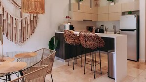 A modern kitchen with a central island, bar stools, and a dining area with a round table and chairs. - 2BR/2BA Luxury Condo in Amira Tulum Pool, Gym & Prime Location (TULUM)