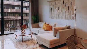 A modern living room with a sofa, a round coffee table, and a macrame wall hanging. - 2BR/2BA Luxury Condo in Amira Tulum Pool, Gym & Prime Location (TULUM)