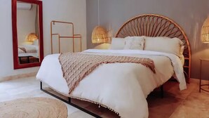A bedroom with a bed, a mirror, a wicker chair, and a lamp. - 2BR/2BA Luxury Condo in Amira Tulum Pool, Gym & Prime Location (TULUM)