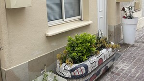 A building exterior with a mailbox, a door, a window with blinds, and a tiled planter with plants. - Apartment T3 DRC cosy climate 2 min beach (Palavas-les-Flots)
