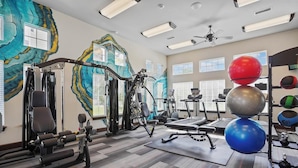 Ett gym med olika typer av träningsutrustning, inklusive styrketräningsmaskiner, löpband och träningsbollar.