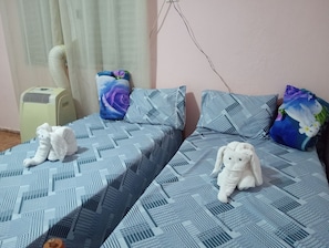 Habitación con dos camas, cada una con ropa de cama estampada, un aire acondicionado de pared y un enchufe.