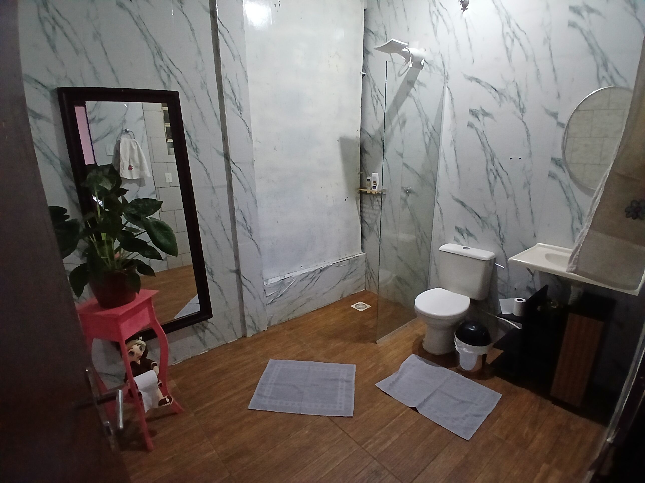 A bathroom with a marble wall, a toilet, a sink, a mirror, and a potted plant.