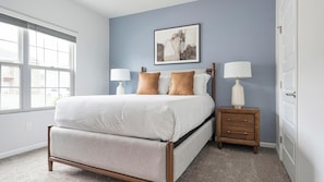 A bedroom with a bed, two bedside tables, a nightstand, a window, and a wall-mounted picture.