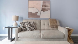 A living room with a sofa, a side table with a lamp, and a framed abstract painting on the wall.
