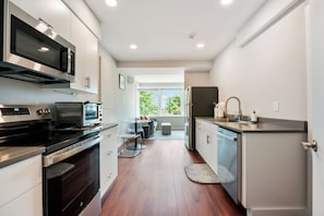 A modern kitchen with stainless steel appliances, a dining area with a glass table, and a view through the window.