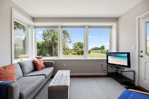 A living room with a grey sofa, ottoman, and a television on a stand.