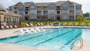 A swimming pool with lounge chairs and a fenced area, surrounded by multi-story apartment buildings. - Landing | Modern 1BD, Gym, Clubhouse (Greer)