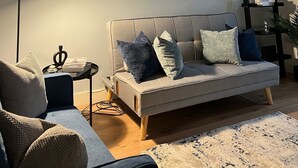 Un salon avec un canapé, une table basse, un lampadaire, un tableau et une bibliothèque.