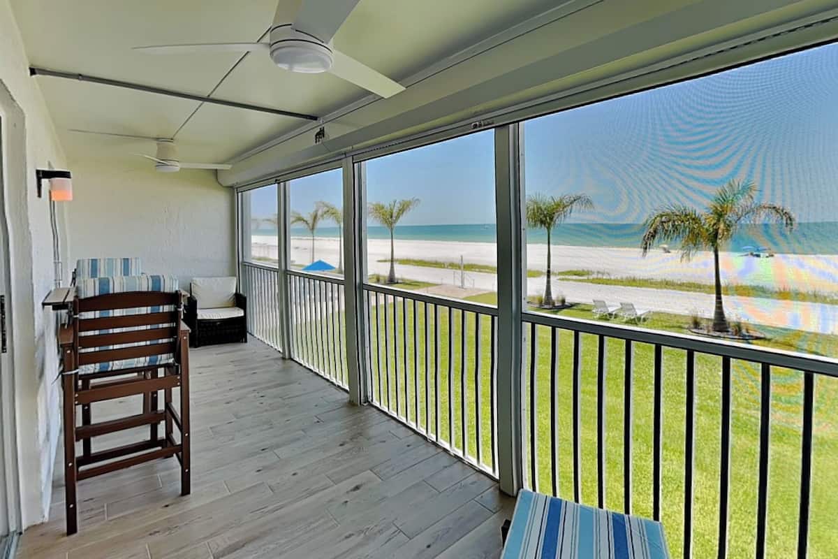A balcony with a view of the beach, a ceiling fan, and a wooden chair.