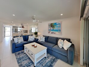 Ein modernes Wohnzimmer mit einem blauen Sofa, einem weißen Couchtisch und einem Gemälde mit einer Strandansicht.