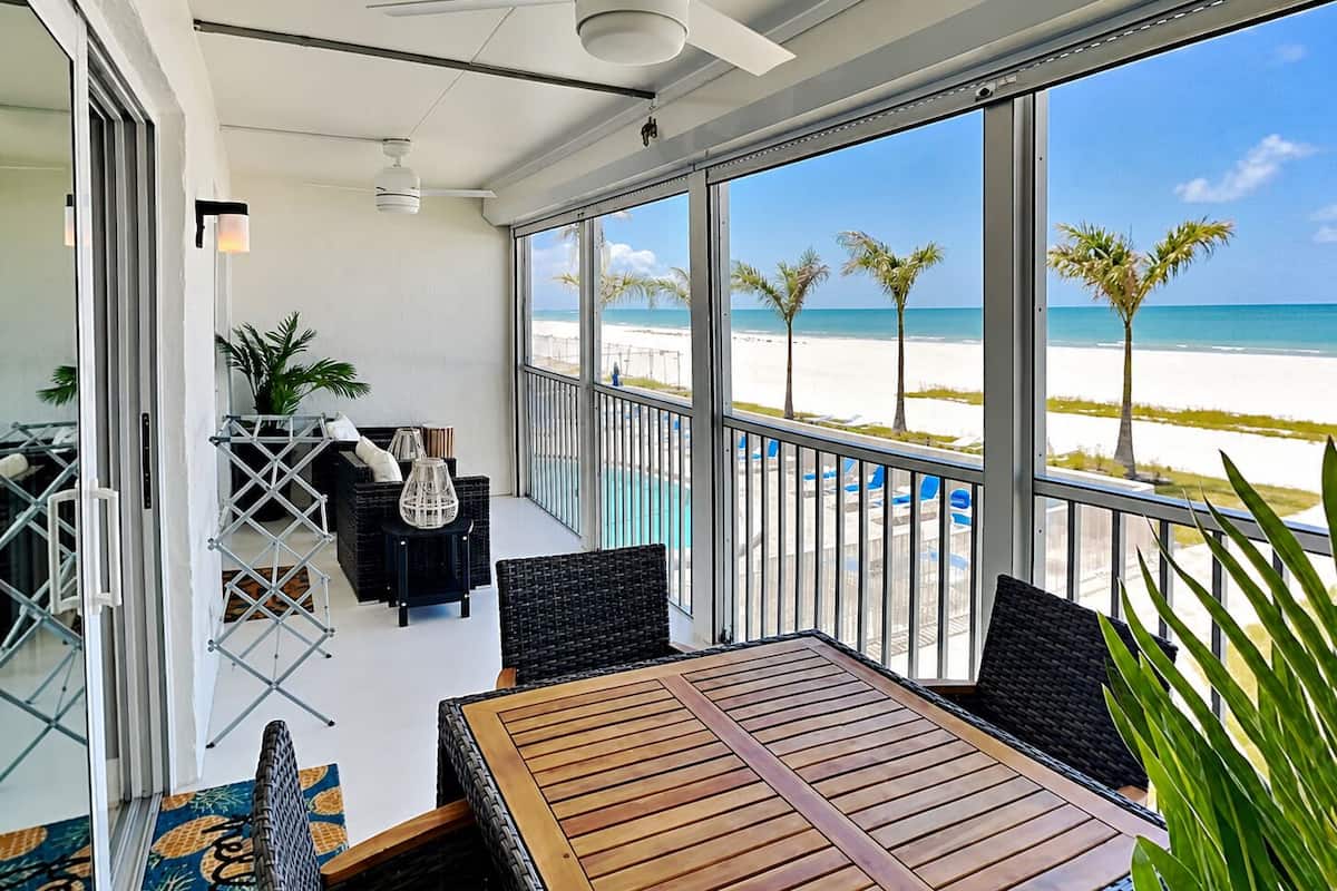 A balcony with a view of the beach, a ceiling fan, and outdoor furniture.