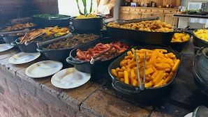 Een buffet met diverse gerechten, een bakstenen muur en een houten kast op de achtergrond.