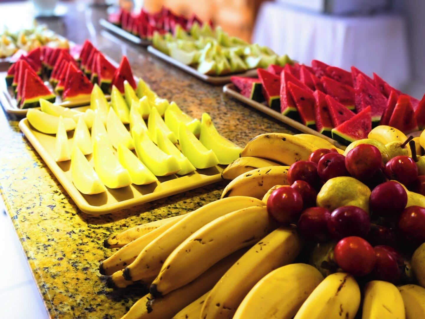 A buffet table with various fruits including bananas, apples, and watermelon slices.