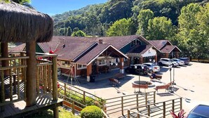 Een resort met rieten hutten, een parkeerplaats en uitzicht op een beboste heuvel.