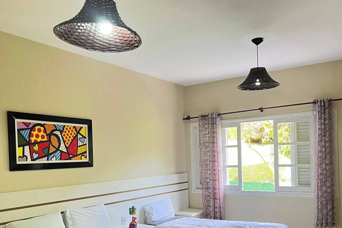 A hotel room with two beds, a large window with curtains, a colorful artwork on the wall, and two pendant lights.