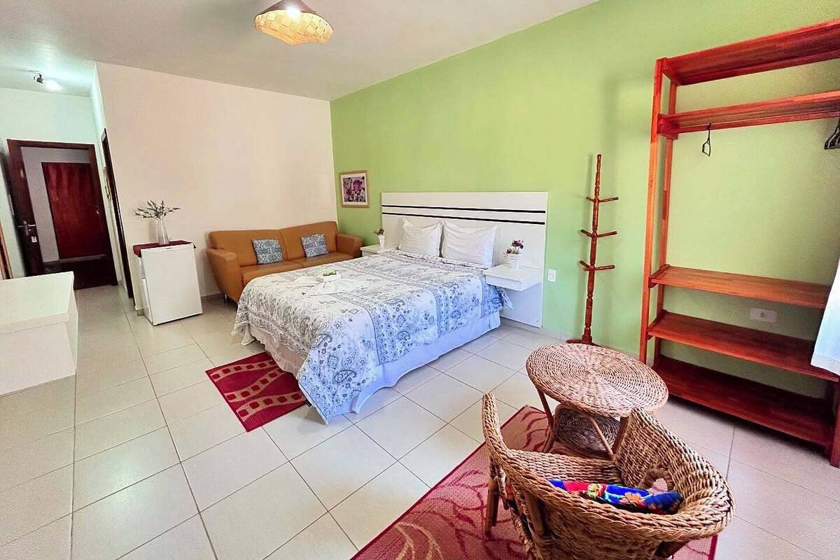 A bedroom with a bed, a nightstand, a chair, a shelf, and a hanging light fixture.