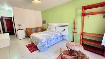A bedroom with a bed, a nightstand, a chair, a shelf, and a hanging light fixture.