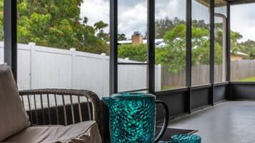 A covered outdoor seating area with wicker furniture, a wooden tray with blue glassware, and a view of the sky and trees.