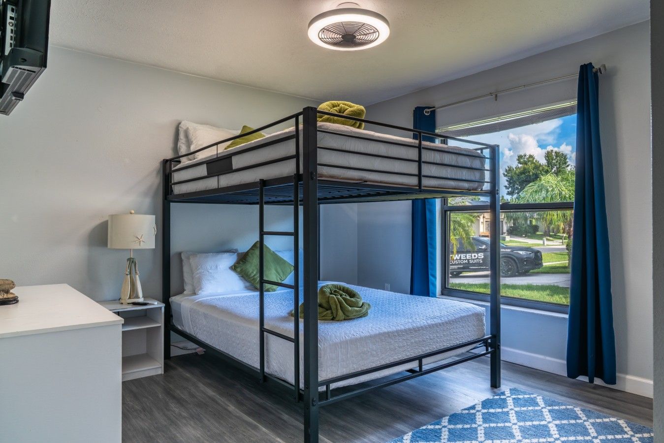 A bunk bed room with a desk, lamp, and a view of the outside.