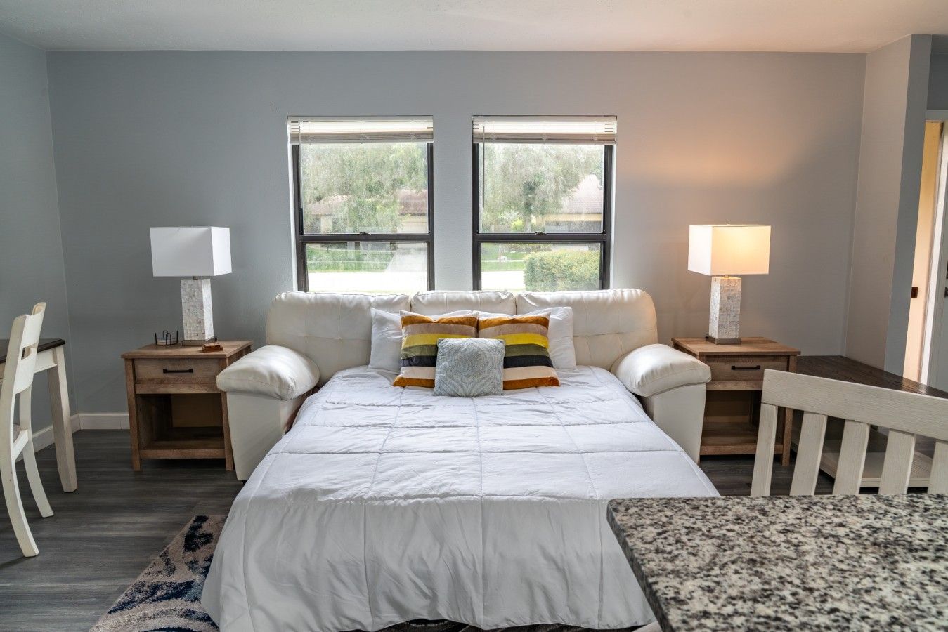 Une chambre à coucher avec un lit, deux tables de chevet, une chaise et deux fenêtres.