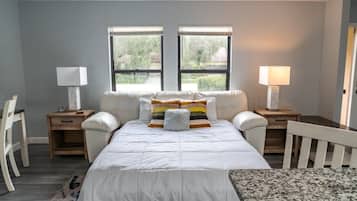 Une chambre à coucher avec un lit, deux tables de chevet, une chaise et deux fenêtres.
