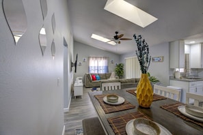 A modern living room with a dining area, a ceiling fan, and a kitchen in the background.