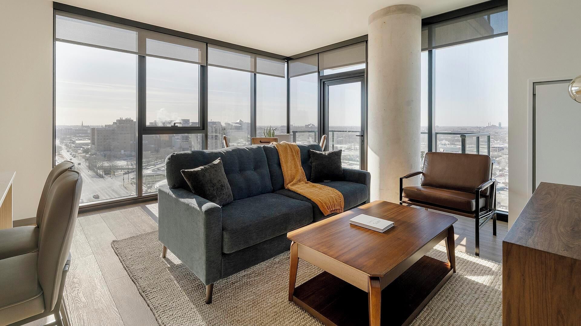 Een moderne woonkamer met een bank, fauteuil, salontafel en grote ramen met uitzicht op de stad.