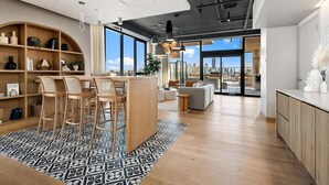 A modern kitchen with a bar area, wooden shelves, and a large window offering a city view. - Landing | Spectacular 1BD, Yoga Studio (Chicago)