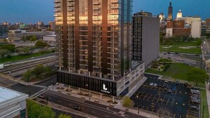 A high-rise building with multiple floors, a parking lot, and a cityscape in the background. - Landing | Spectacular 1BD, Yoga Studio (Chicago)