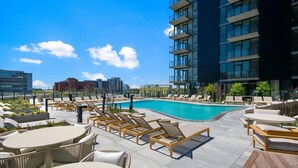 A rooftop pool area with lounge chairs and tables, a swimming pool, and modern buildings in the background. - Landing | Spectacular 1BD, Yoga Studio (Chicago)