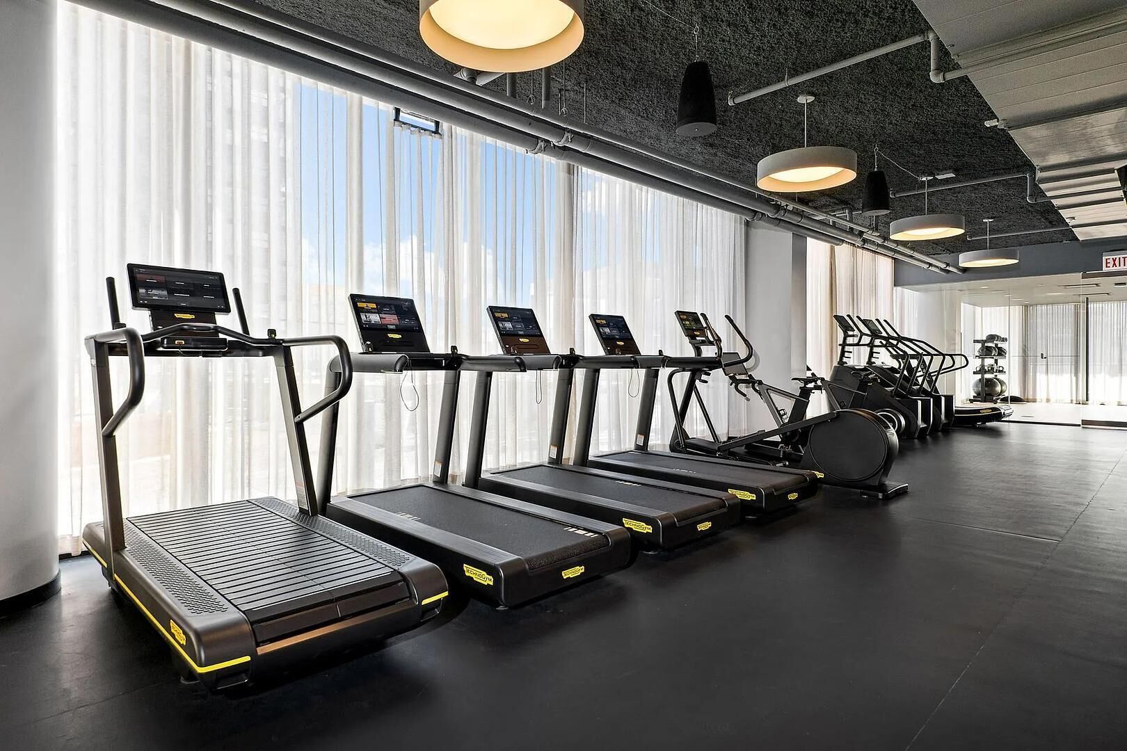 Ein Fitnessstudio mit Laufbändern, Crosstrainern und einem Krafttrainingsgerät.