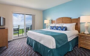 A hotel room with a bed, two bedside lamps, a television, a wooden nightstand, and a sliding glass door leading to an outdoor area with chairs. - Whale Watching, Ocean Views, 3 Bedroom Condo in beautiful Depoe Bay - sleeps  8 (Depoe Bay)