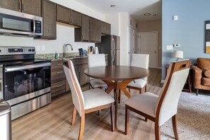 A modern kitchen with stainless steel appliances, wooden cabinets, and a dining area with a round table and four chairs. - Landing | Incredible 2BD, Gym, Pool (Spartanburg)