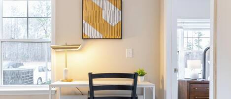 Una stanza con scrivania, sedia, lampada e un quadro astratto appeso al muro.