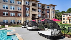 A hotel with a swimming pool, outdoor seating with wicker chairs and cushions, and a brick facade. - Landing | Spectacular 2BD, Game Room, Pool (Spartanburg)
