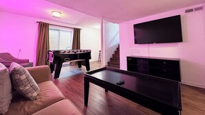 A living room with a foosball table, a sofa, a coffee table, a TV, and a staircase. - Sleeps 8 • Pet Friendly • Near Mall of America (Saint Paul)