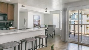 Een moderne keuken met een centraal eiland, barstoelen, een eethoek met stoelen en een glazen schuifdeur naar een balkon.