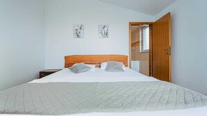 A bedroom with a large bed, a wooden headboard, two wall-mounted artworks, a nightstand, and a wooden door leading to a bathroom. - Seaview apartment Verde near beach (Okrug Gornji)