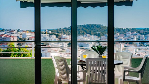 A balcony with a table and chairs, a potted plant, and a view of a cityscape. - Seaview apartment Verde near beach (Okrug Gornji)